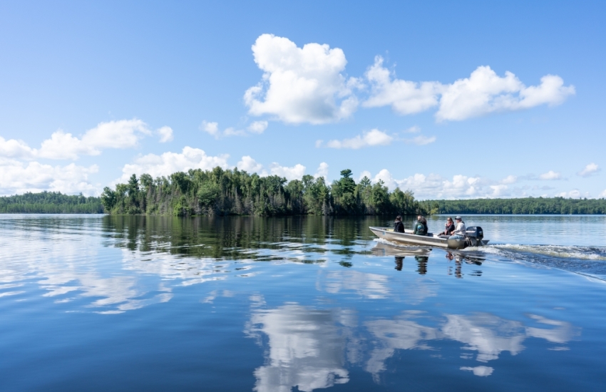 A motorboat cruises along Escanaba Lake on a bright, sunny day with clouds reflecting in the water.