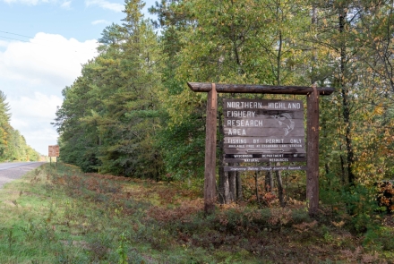 A wooden sign that says Northern Highland Fishery Research Area by a road. 