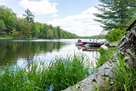 A boat floats in the water at the Nebish Lake boat launch with sunny skies overhead.