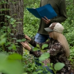 Two young adults check a trail camera.