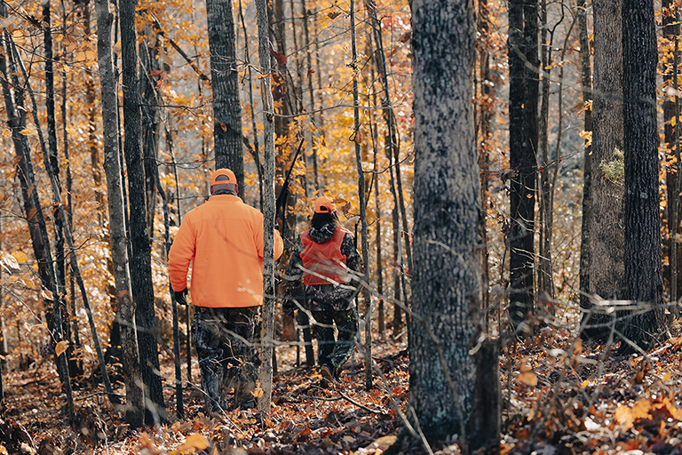 Two hunters walking in the woods during fall hunting season.