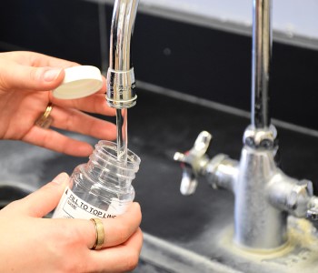 A person filling a lab test bottle with water from a running tap.