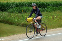 Woman riding a bike past a farm field even in a light rain