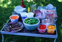 an outdoor table full of chopped vegetables and other food items