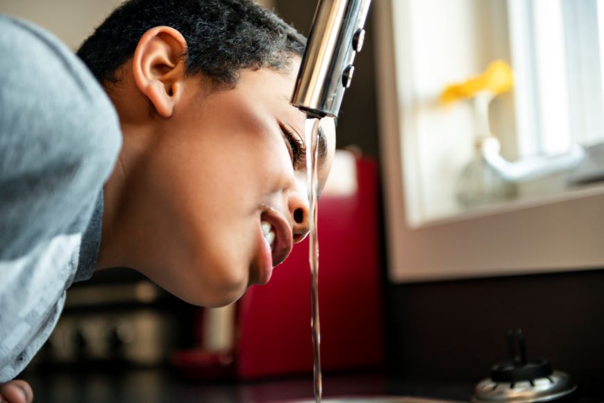 A child leaning over the sink drinking water from the tap